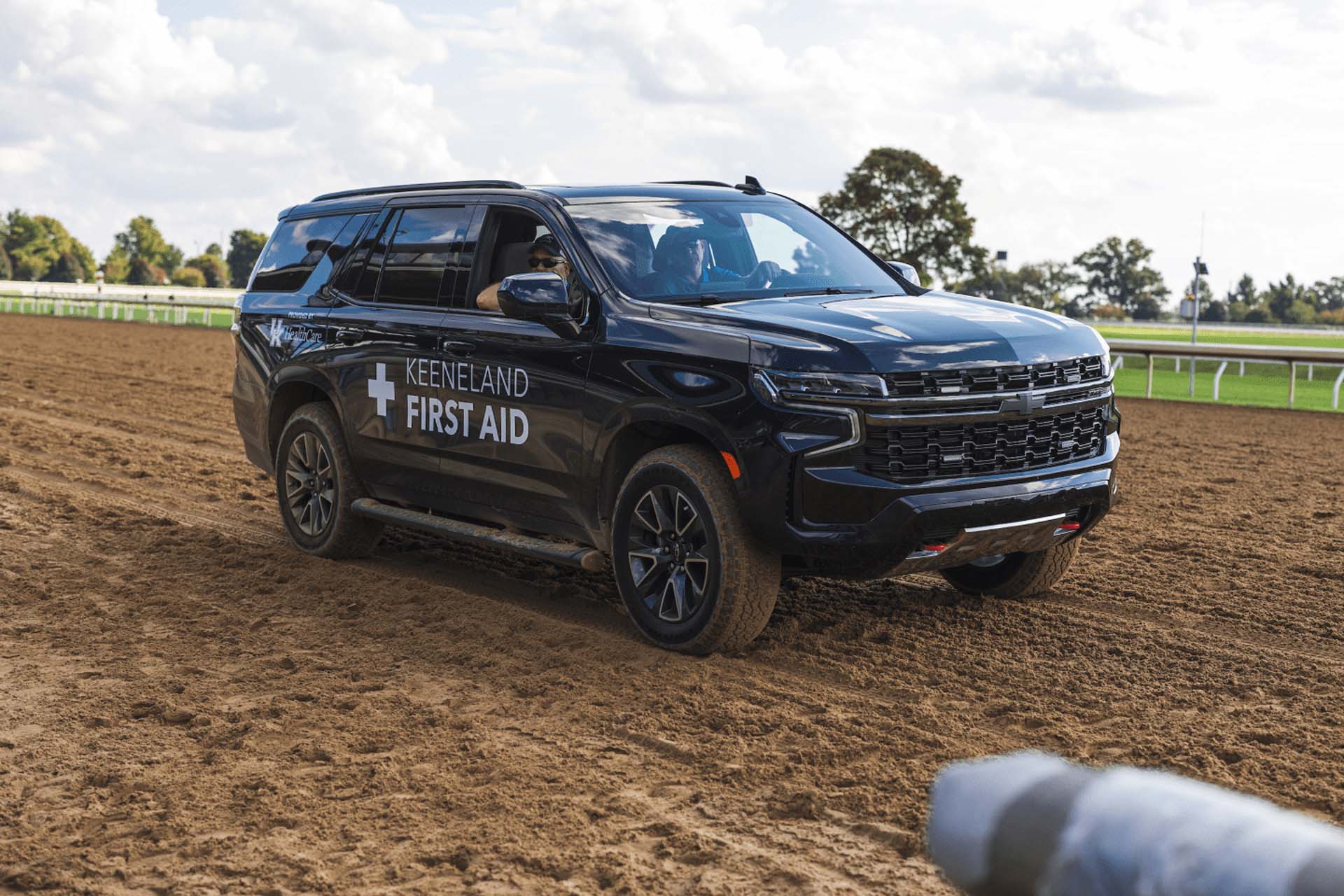 A picture of the Racetrackwin First Aid car on the dirt track. It is a large black Chevy SUV.